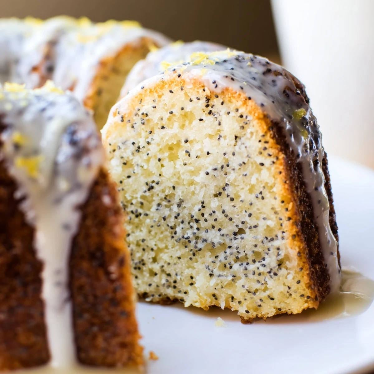 Lemon Poppy Seed Bundt Cake displayed on a white ceramic platter with fresh lemon slices and powdered sugar for a bright dessert presentation.