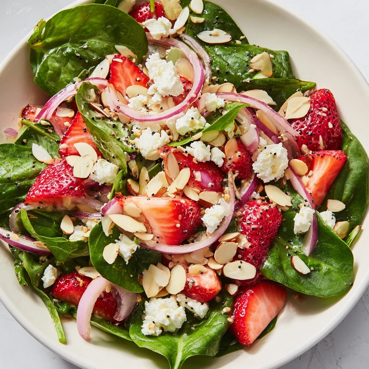 A close-up of vibrant red strawberries, green spinach, and creamy feta cheese drizzled with homemade poppy seed dressing on a rustic wooden table.  