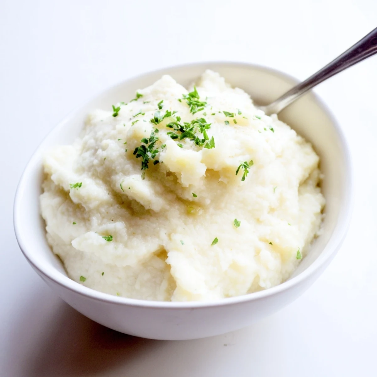 A creamy serving of Roasted Garlic Mashed Cauliflower garnished with fresh green chives, a low-carb side dish.
