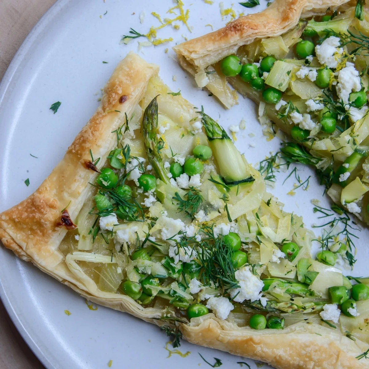 A rustic Spring Vegetable Galette with Goat Cheese cooling on a rack, with fresh herbs sprinkled on top and a slice ready to be served.