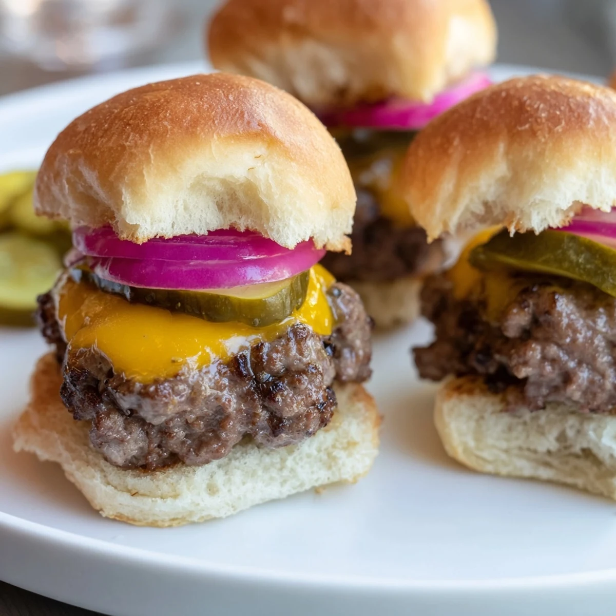 A close-up of Beef Sliders with Cheese and Pickles, garnished with thin red onion slices and served alongside golden fries on a casual dinner table.