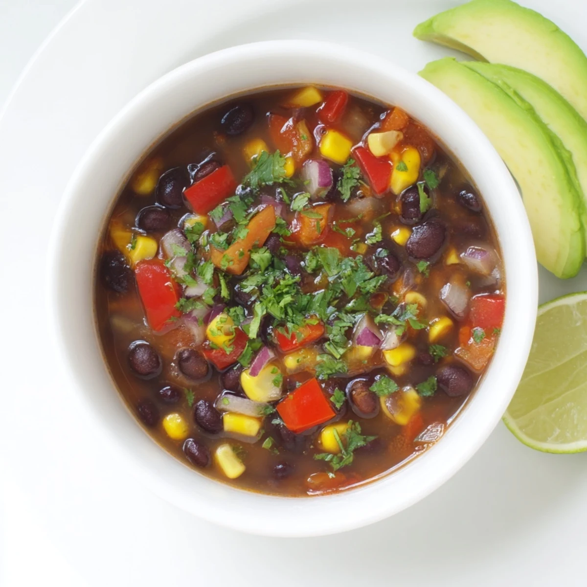 A steaming bowl of Black Bean Corn Chili Lime Delight garnished with fresh cilantro and lime wedges.