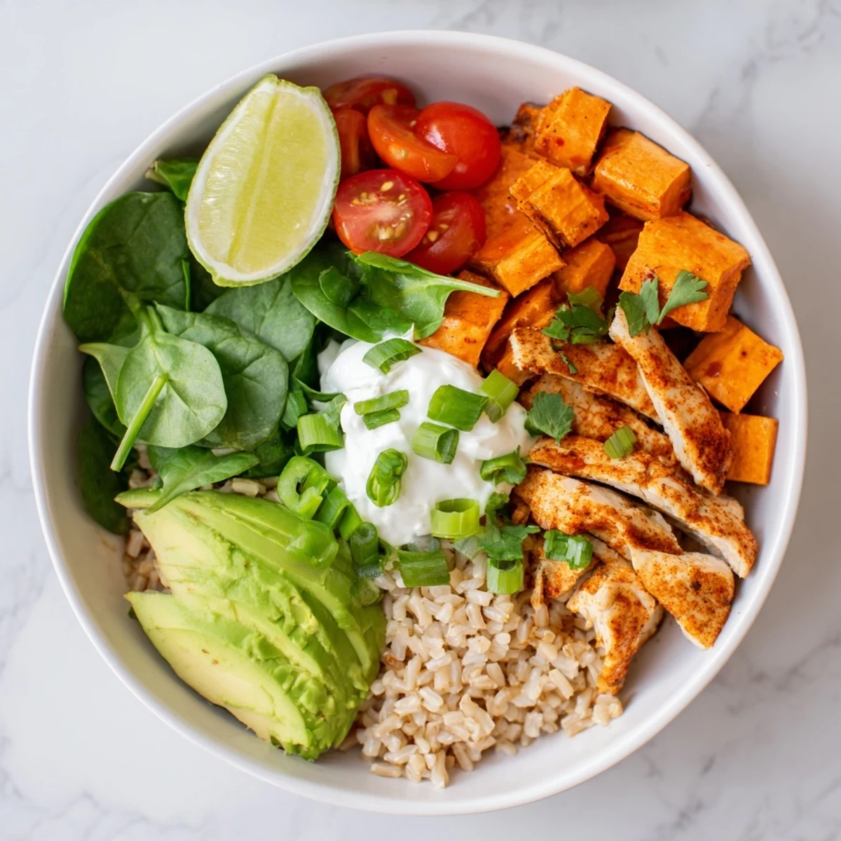 A close-up of the wholesome chicken sweet potato rice bowl shows juicy chicken, tender roasted sweet potatoes, and vibrant cherry tomatoes with a creamy dollop of Greek yogurt.