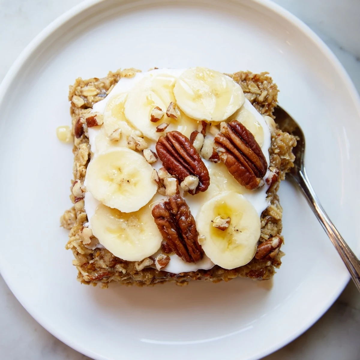 A warm slice of Banana Baked Oatmeal with Greek Yogurt served with a generous dollop of creamy yogurt and drizzle of maple syrup.
