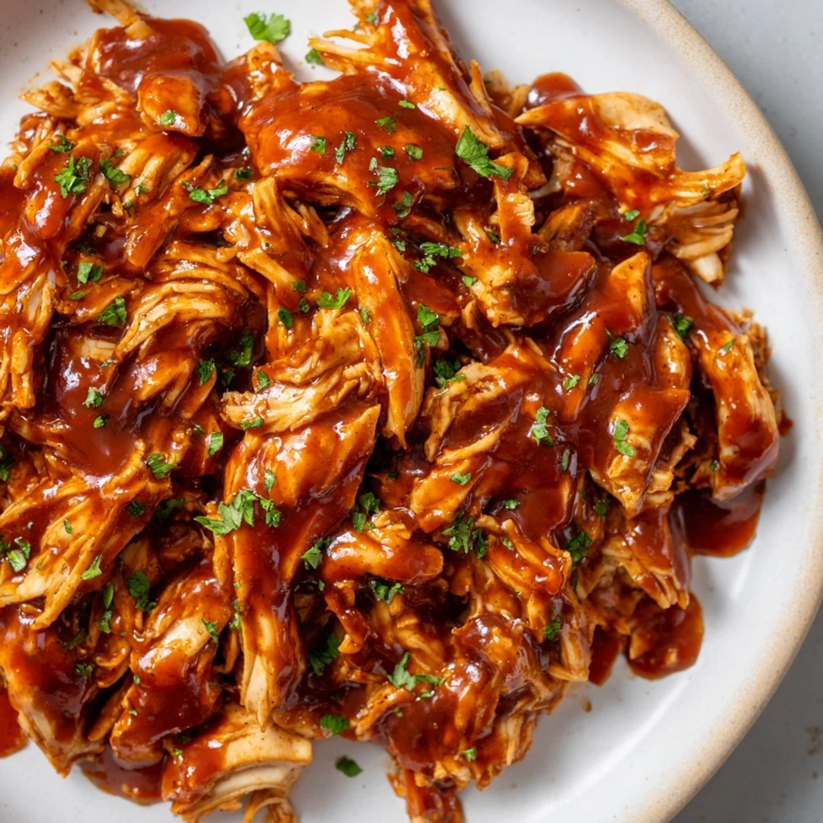 Garnished with fresh parsley, this slow-cooked Sweet Baby Rays Crockpot Chicken is served on a warm bun for a delicious dinner.