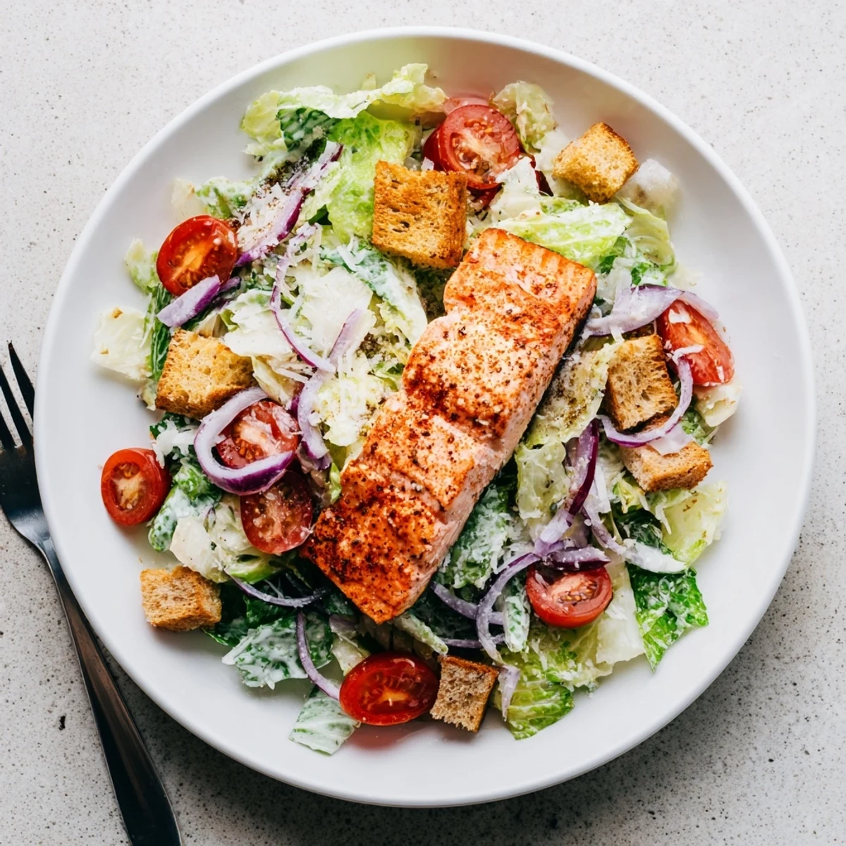 Flaky salmon Caesar salad features fresh greens, homemade dressing, and shaved Parmesan on a white plate