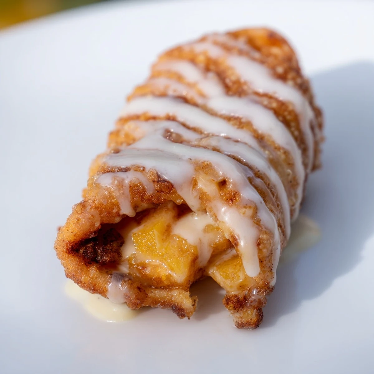 Golden peach cobbler egg rolls drizzled with vanilla glaze on a white plate