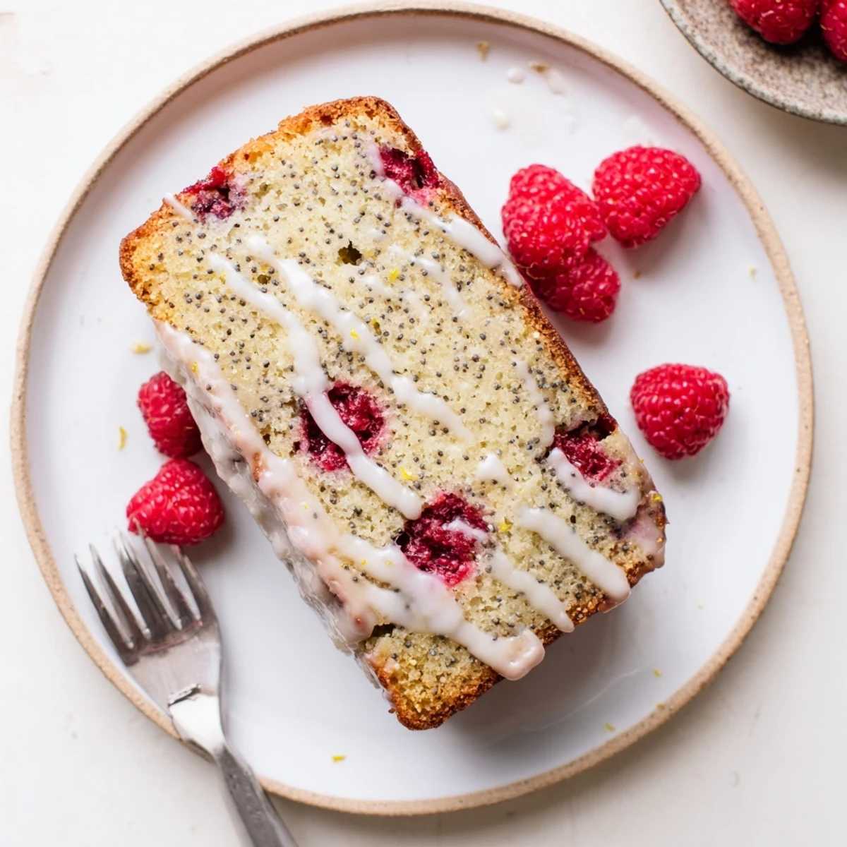 Golden raspberry lemon poppyseed loaf cake drizzled with white lemon glaze on a white serving plate