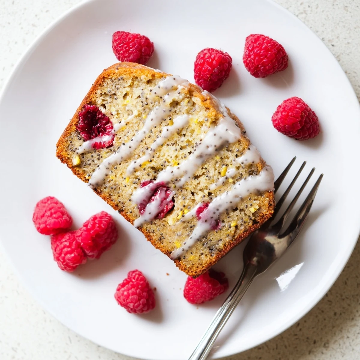 Fresh raspberries peek through moist lemon poppyseed loaf cake slices arranged on a wooden cutting board