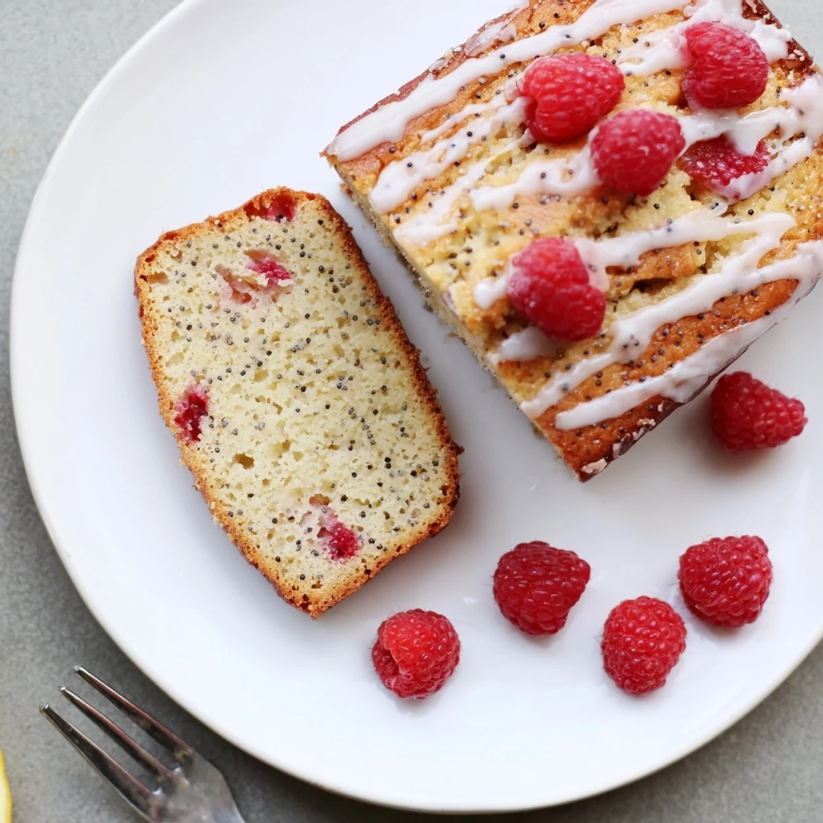 Glazed raspberry lemon poppyseed loaf cake with whole raspberries and lemon zest garnish on rustic platter