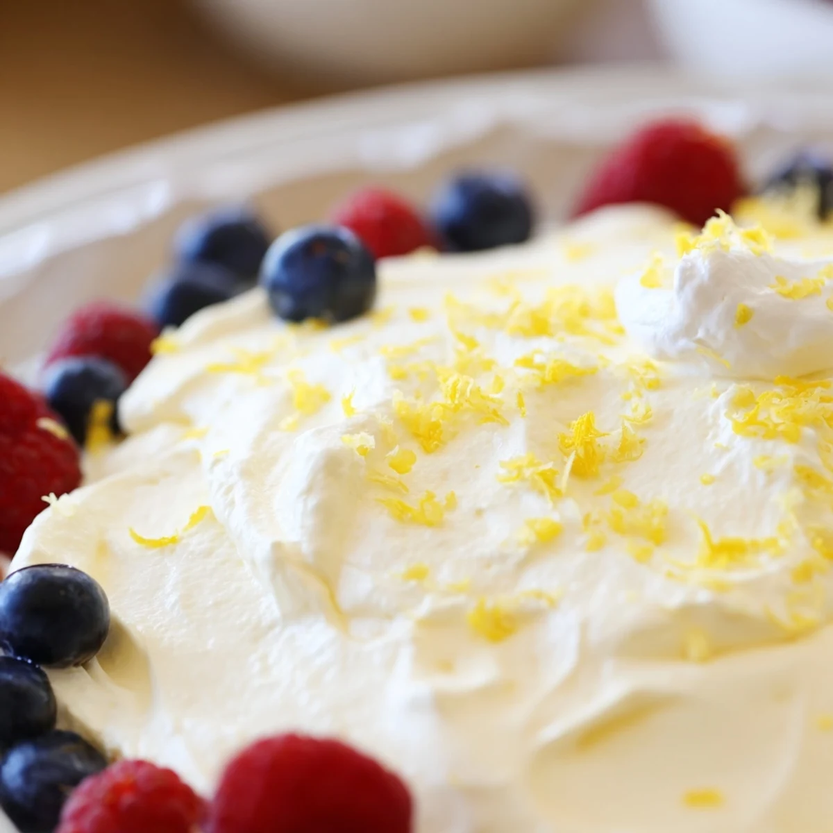 Creamy lemon cheesecake mousse topped with fresh berries and graham cracker crumbs in clear glass