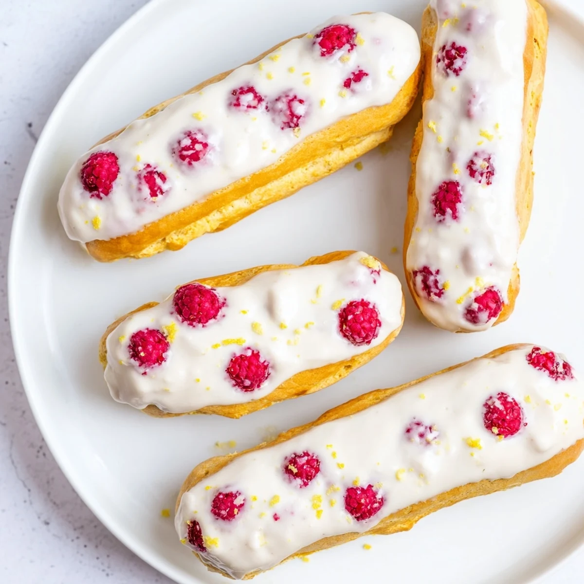 Golden lemon raspberry éclairs filled with tangy lemon cream and topped with light lemon glaze