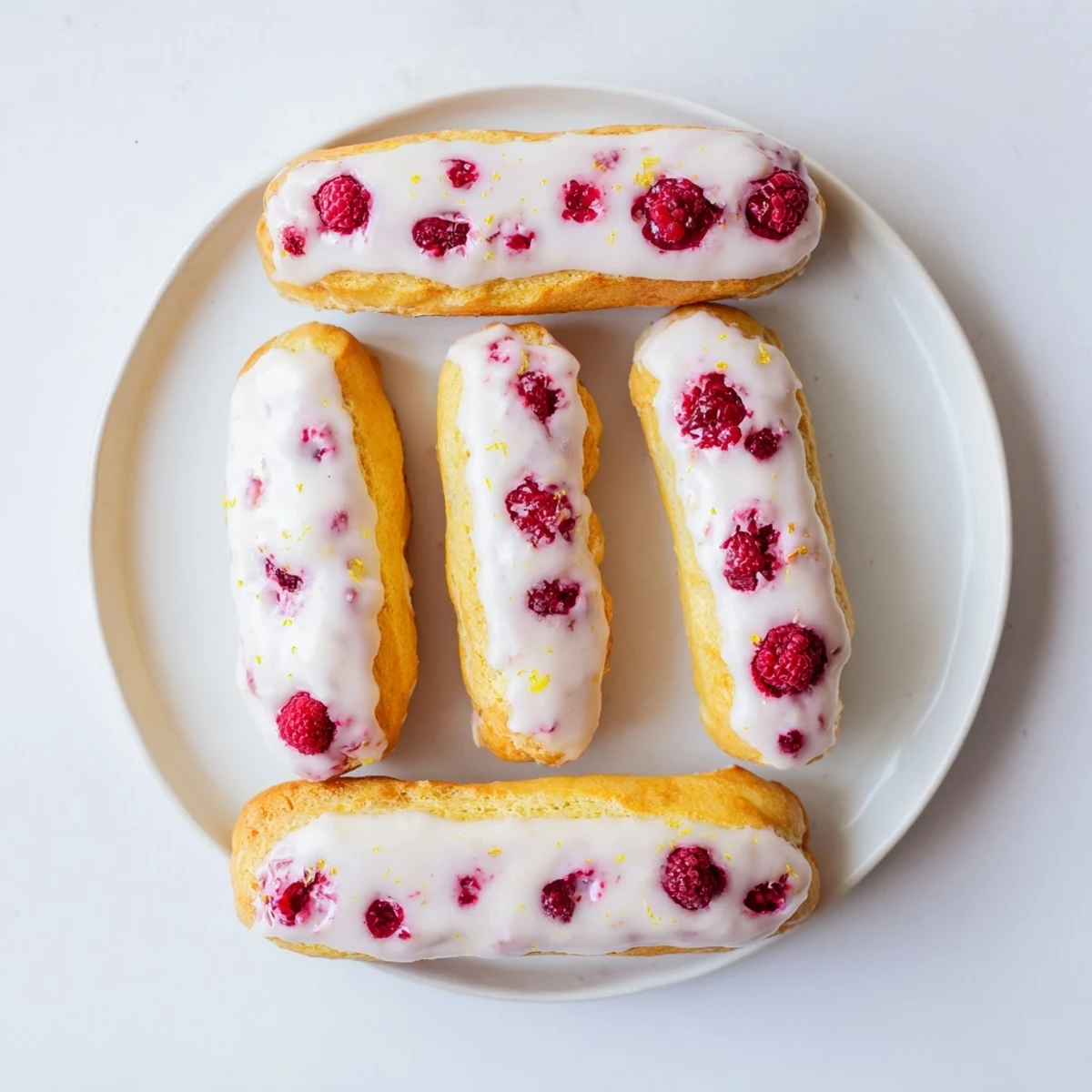 Elegant dessert plate displaying three glazed lemon raspberry éclairs with smooth cream and berry filling