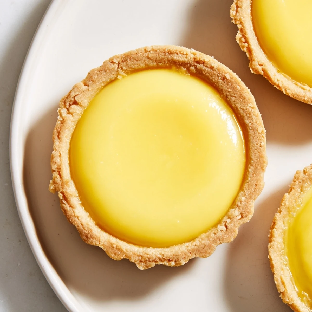 Bite-sized vegan lemon tarts topped with fresh lemon zest, arranged on a wooden board for dessert presentation