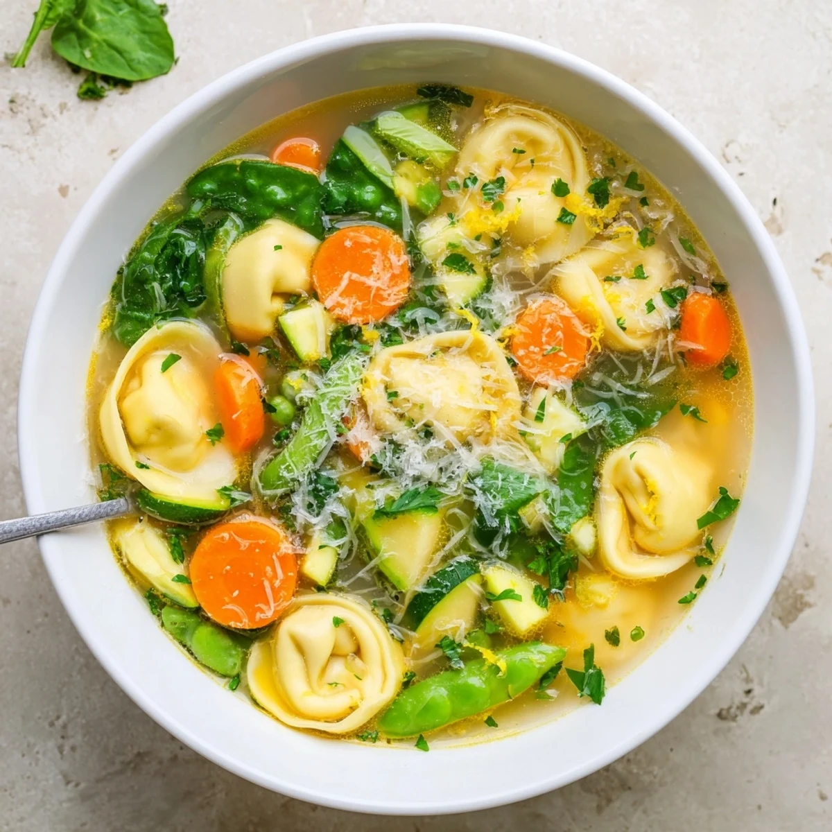 Steaming bowl of spring tortellini soup with tender vegetables and floating cheese pasta pieces