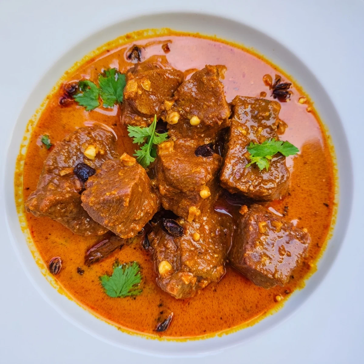 Rich spicy beef curry garnished with fresh cilantro over steaming white basmati rice
