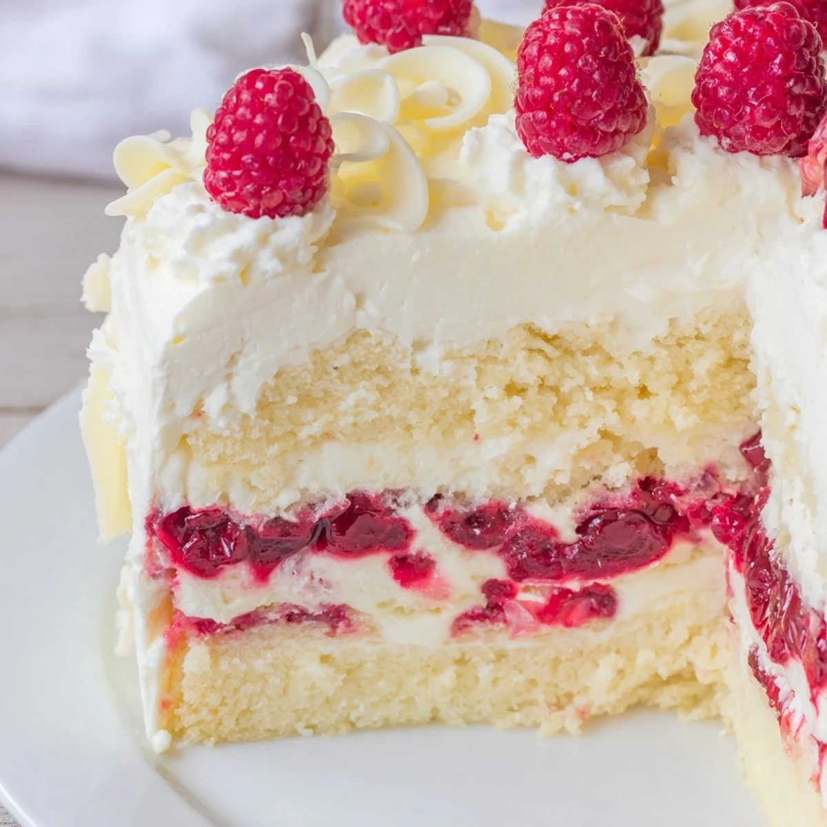 Slice of white chocolate raspberry cream cake showcasing layers, fruity compote, and fluffy whipped cream topping