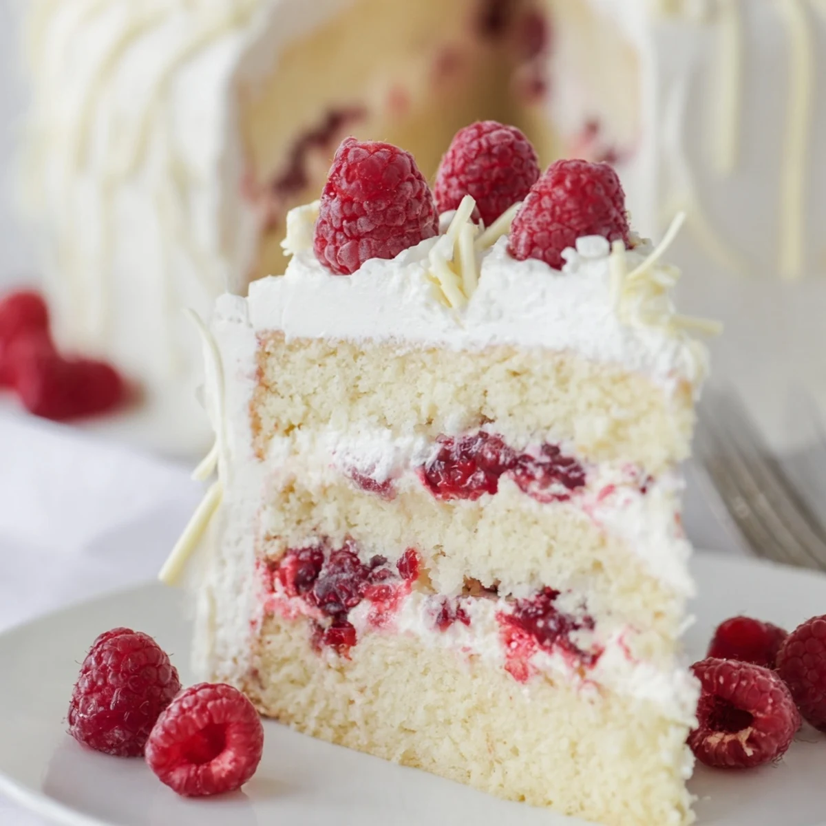 Layered white chocolate raspberry cream cake with ruby red compote between vanilla sponge and cream frosting