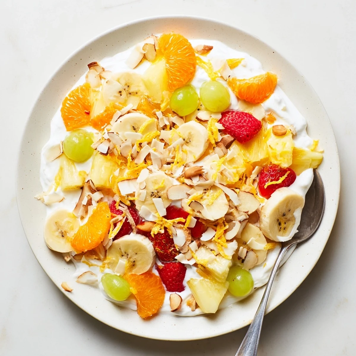 Colorful bowl of creamy fruit salad featuring fresh strawberries, pineapple, and grapes coated in tangy yogurt dressing