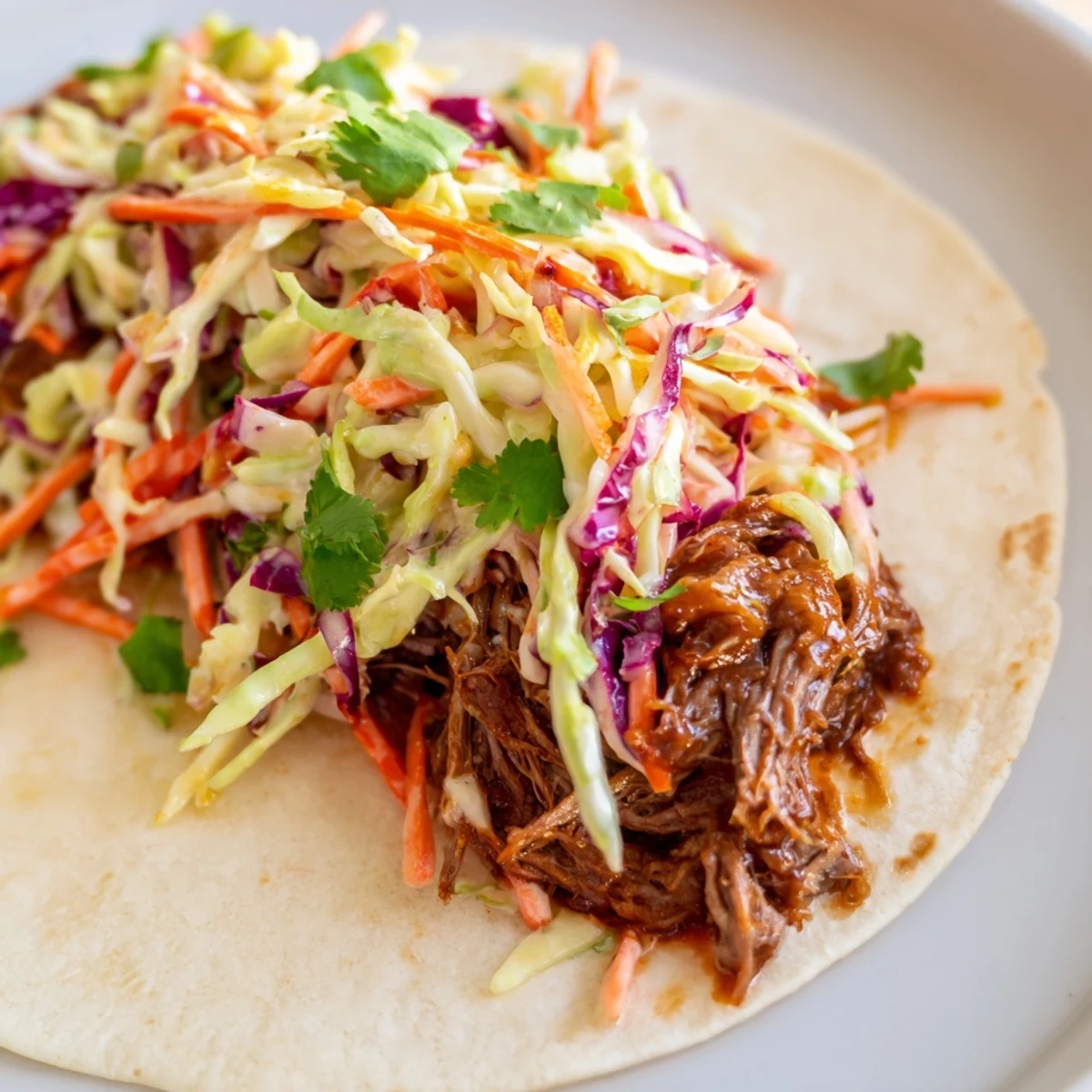 Tender BBQ pulled beef wrapped in soft flour tortillas with colorful crunchy slaw and fresh herbs