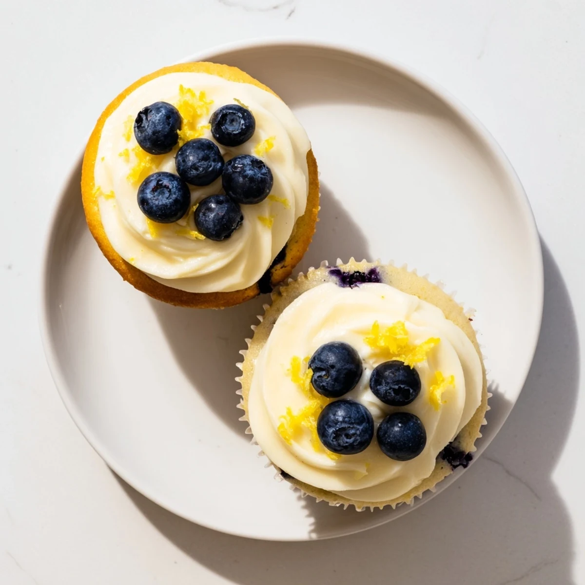 Golden lemon blueberry cupcakes topped with fluffy white cream cheese frosting and fresh blueberries