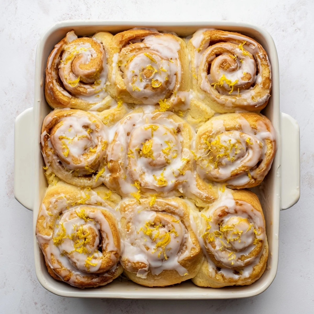 Freshly baked lemon rolls glazed with tangy icing and garnished with bright lemon zest