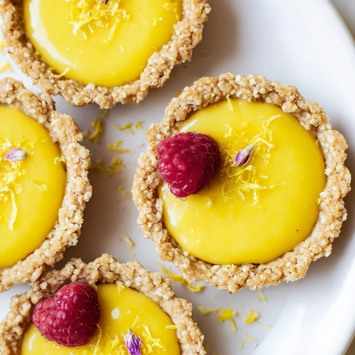 Golden mini vegan lemon tarts topped with fresh berries on a rustic white serving board