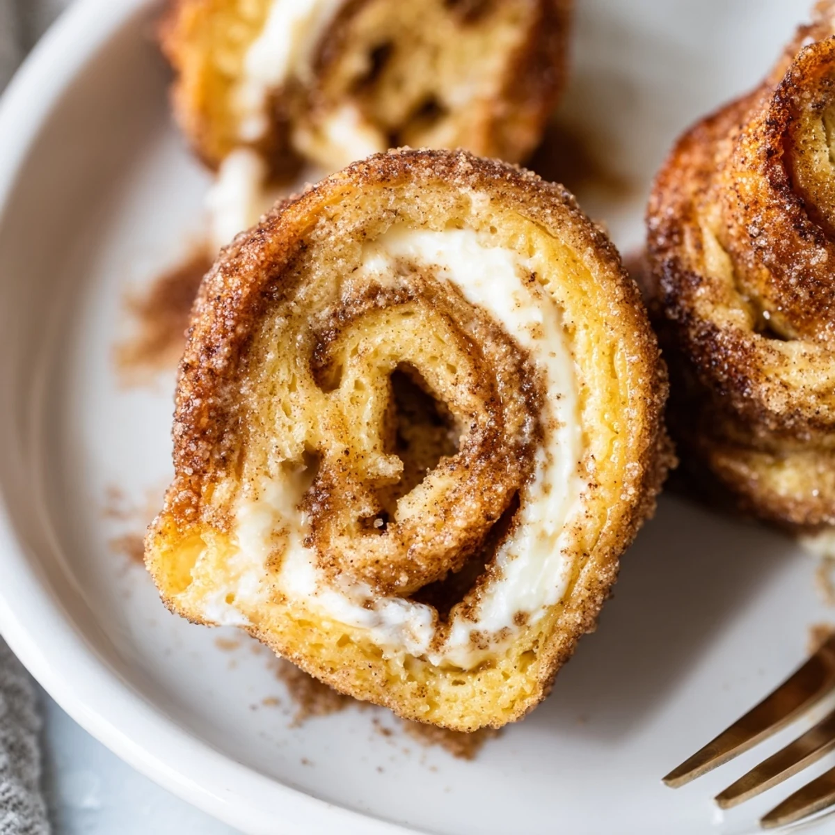 Cinnamon Roll French Toast Roll Ups golden, sugar-coated, steaming on a plate