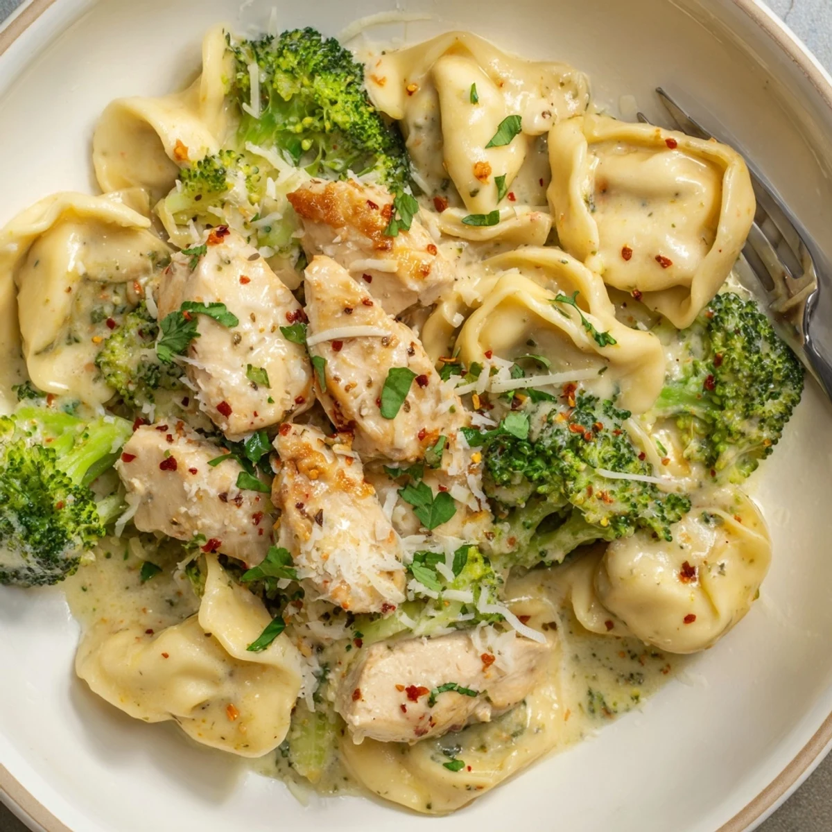 Fork lifting cheesy bite from Creamy Garlic Parmesan Tortellini Chicken Broccoli Recipe, buttery sauce