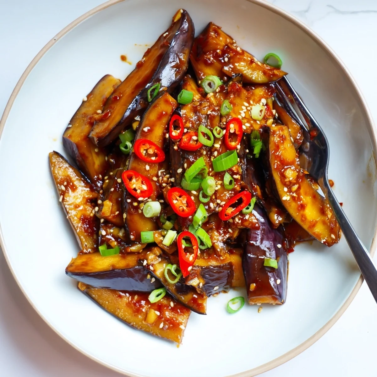 Glistening Sichuan Style Braised Aubergines in spicy red sauce, scallions garnish.