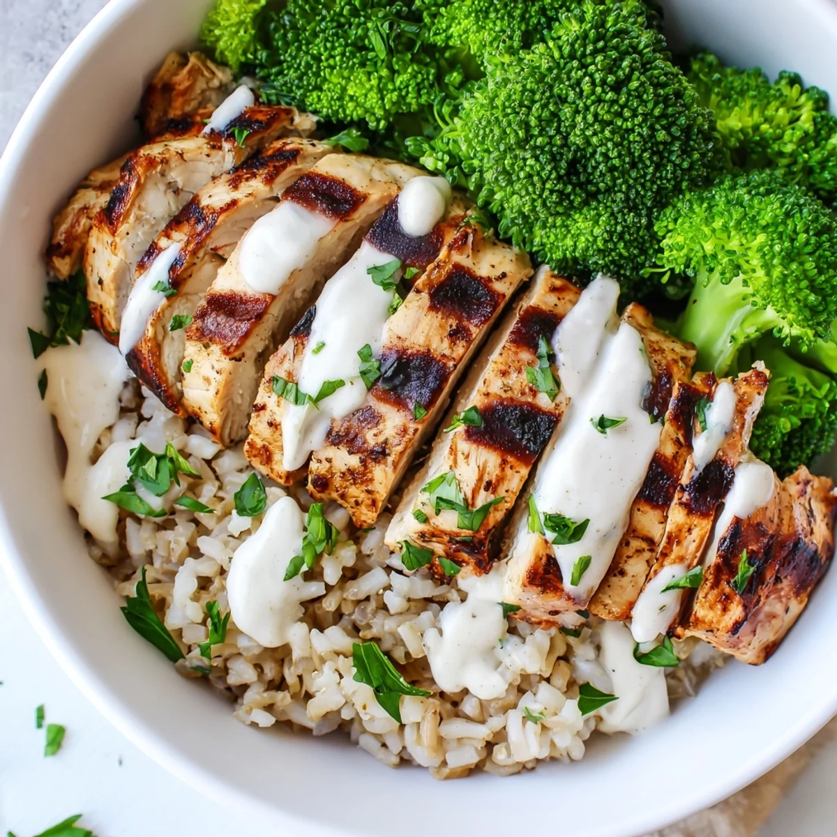 Healthy grilled chicken broccoli bowls topped with creamy garlic sauce over rice