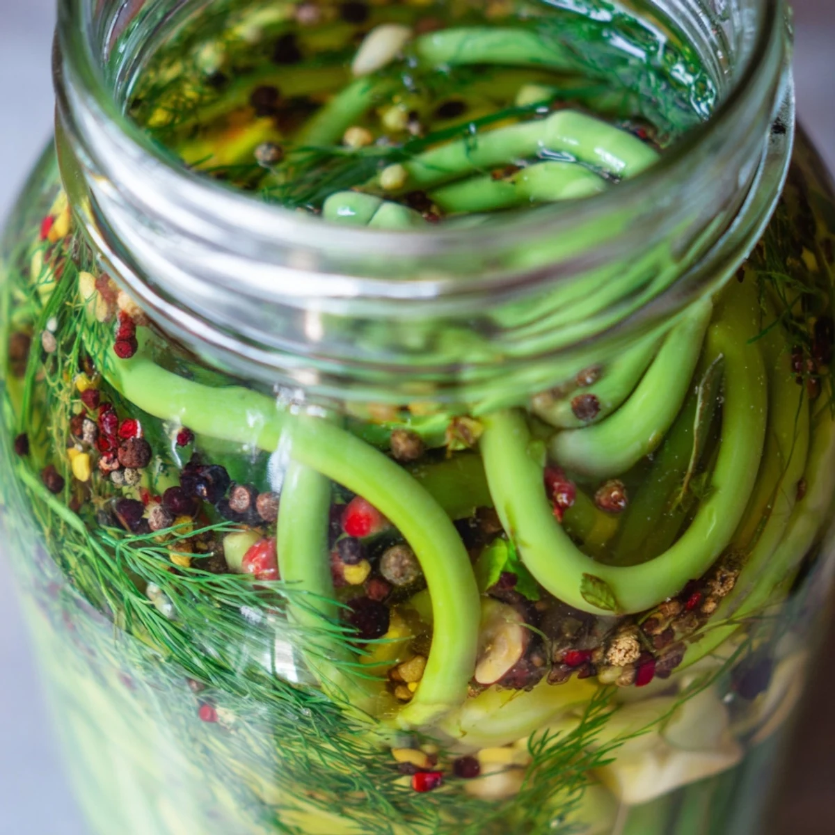 Close-up of crunchy garlic scapes curing in spiced vinegar brine with mustard seeds and whole dried chilies for extra heat