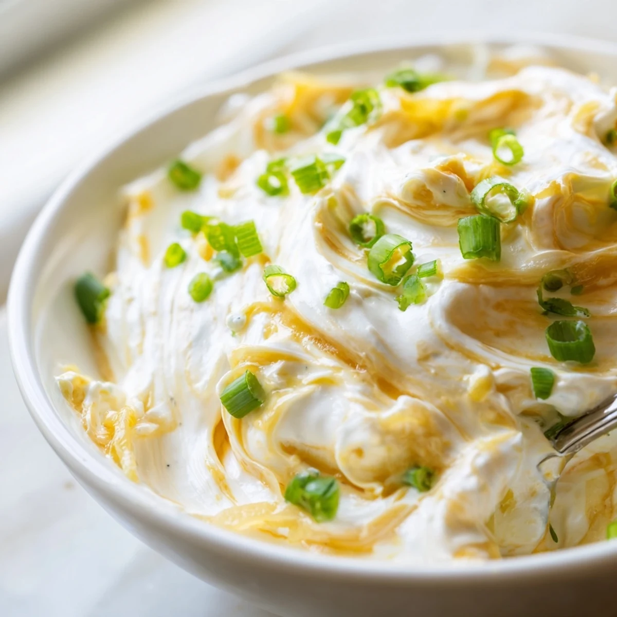 Creamy French onion dip topped with caramelized onions and fresh green onions, served in a white bowl with crispy potato chips surrounding it
