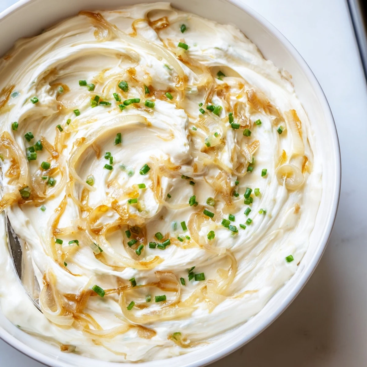 Golden brown caramelized onions swirled into a rich, creamy French onion dip garnished with chives and paired with vegetable crudités for dipping