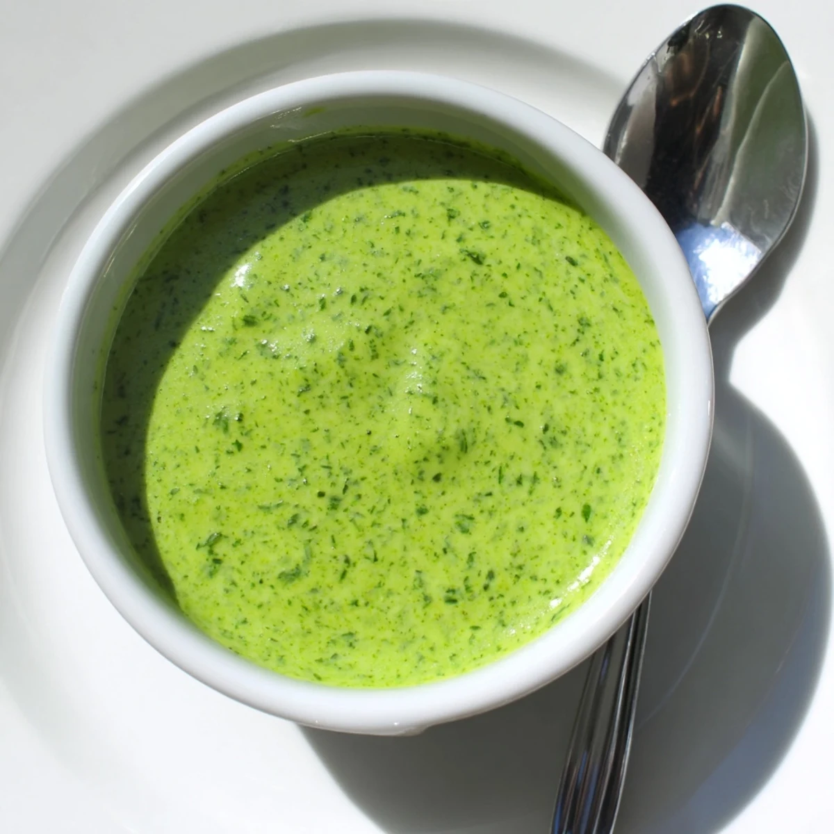 Bright green cilantro lime sauce served in small white dipping bowl beside tortilla chips