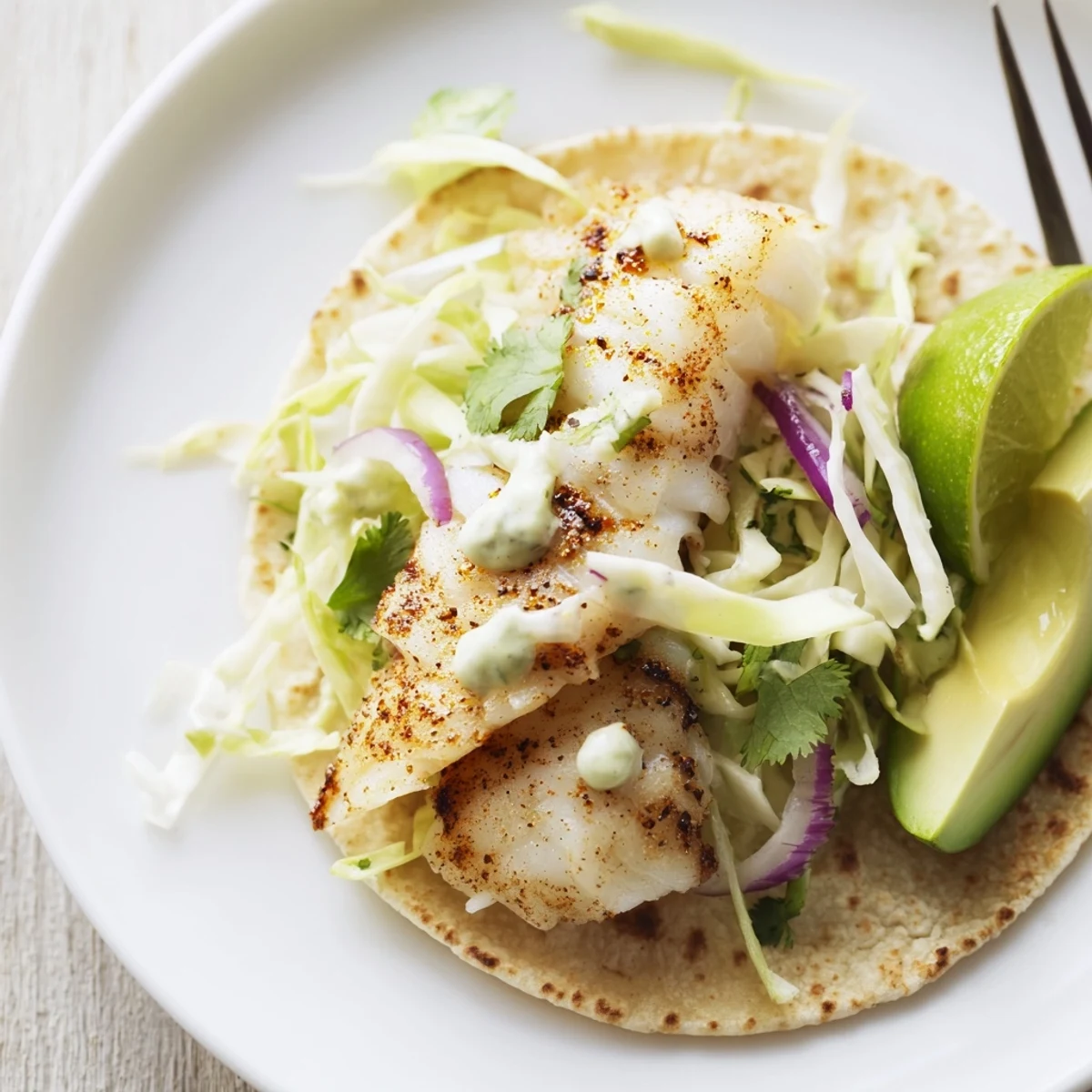 Baked Cod Fish Tacos with Creamy Cilantro Lime Sauce drizzled, avocado slices and lime