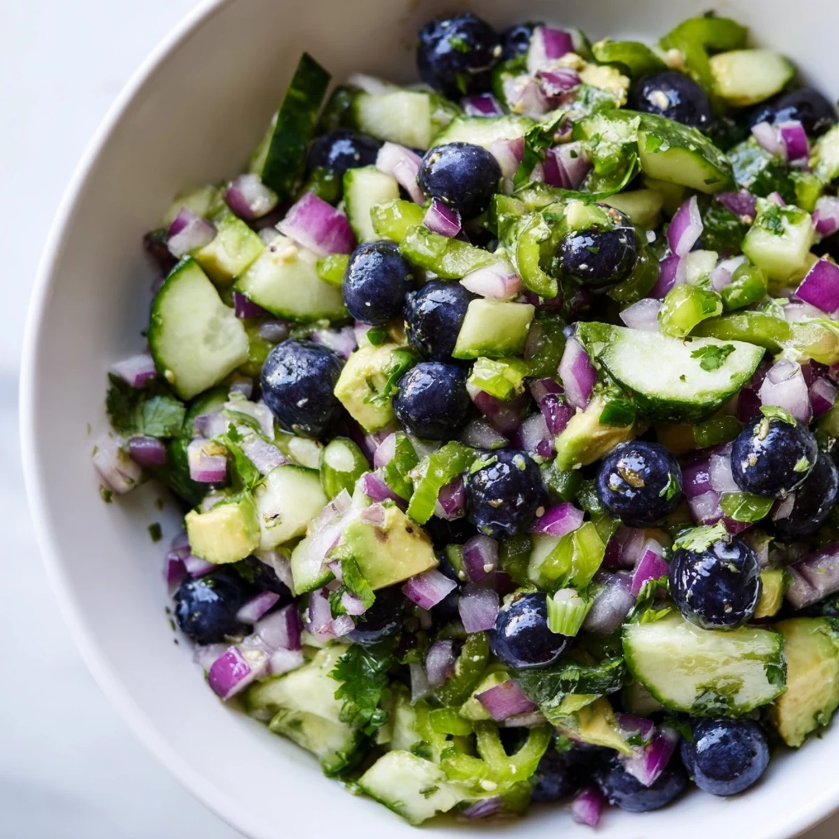 A close-up of blueberry cucumber salsa in a white bowl with tortilla chips nearby