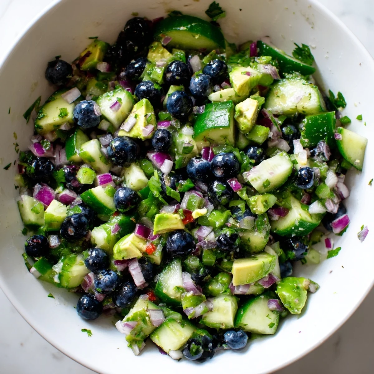 Vibrant blueberry cucumber salsa spooned into a glass dish garnished with fresh herbs