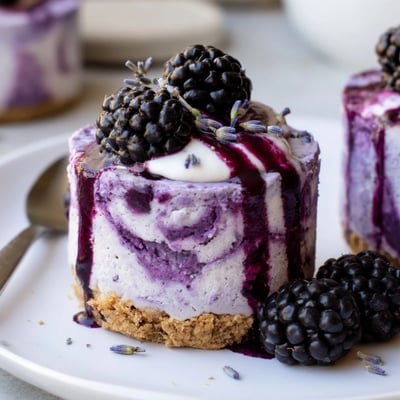 Velvety blackberry lavender cheesecakes with buttery graham crust drizzled in berry sauce